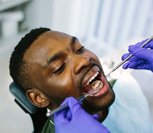 Male dental patient receiving checkup from dentist wearing gloves