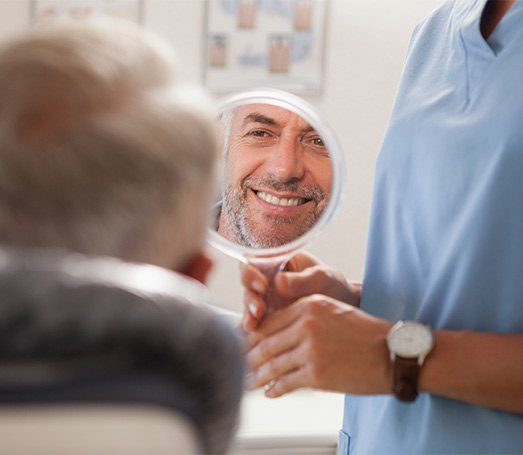 Man smiling at reflection in handheld mirror