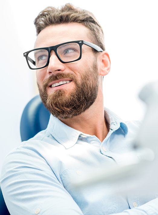 Man with glasses smiling in dental chair after full mouth reconstruction in Los Angeles