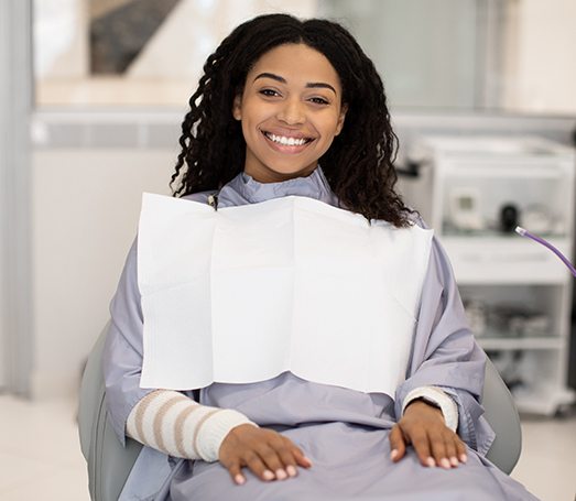 Smiling woman sitting in dental chair with hands on lap