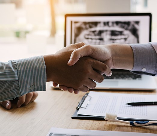 Close-up of patient and dentist shaking hands over desk